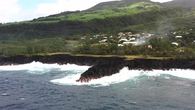 Aerial drone view of Puits des Francais on a stormy day with high breaking waves, cliffs and mountain range in the background, Saint-Philippe, Reunion.
