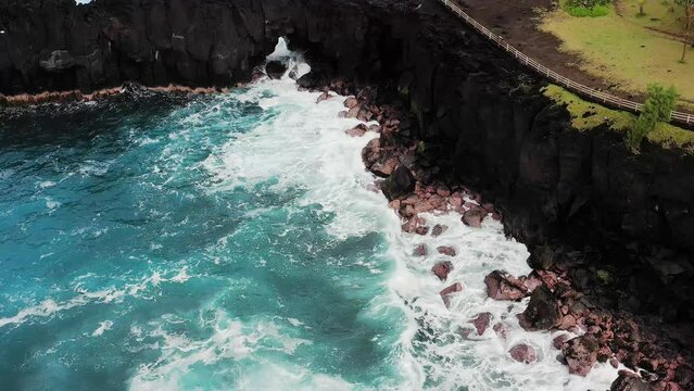 Aerial drone view of Puits des Francais on a stormy day with high breaking waves, cliffs and mountain range in the background, Saint-Philippe, Reunion.