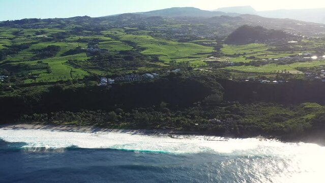 Aerial drone view of Puits des Francais on a stormy day with high breaking waves, cliffs and mountain range in the background, Saint-Philippe, Reunion.