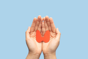 World Thyroid Day concept. Human hand holding thyroid gland shape made from paper on blue background. Awareness of thyroid disease such as hyperthyroidism, hypothyroidism and thyroiditis. - obrazy, fototapety, plakaty