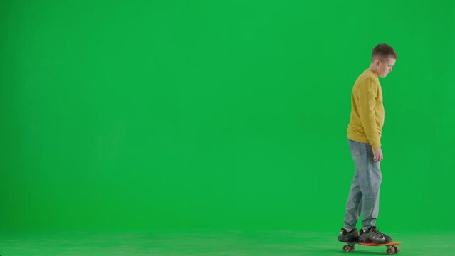Portrait of boy on chroma key green screen. School boy kid in casual clothing riding on skateboard from left to right in the frame, happy face.