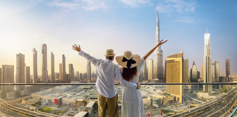 A happy tourist couple on vacation time stands on a balcony and enjoys the panoramic view of the Dubai city skyline, UAE - obrazy, fototapety, plakaty