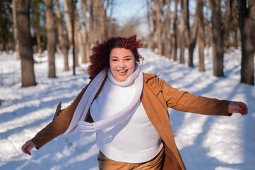 Portrait of an excited red-haired curly fat woman in the park in winter.