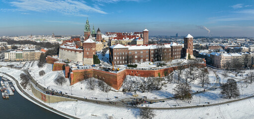 Krakow, Poland. Royal Wawel Cathedral and castle covered with snow in winter. Vistula river and tourist boats. Aerial panorama with boulevard, promenades and walking people. Old city in the background - 689673413