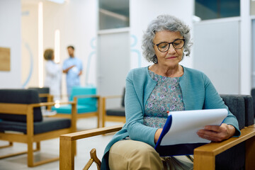 Mature woman filling out medical paperwork while sitting in waiting room at doctor's office.