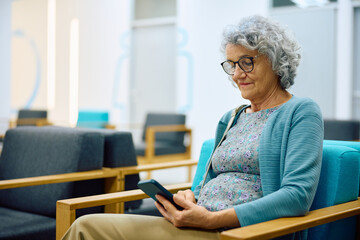 Senior woman using cell phone in waiting room at doctor's office.