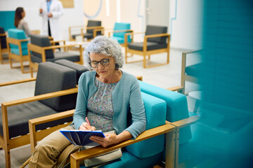 Senior woman filling out medical papers in waiting room at clinic.