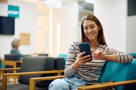 Happy woman texting on mobile phone while waiting for medical appointment at clinic.