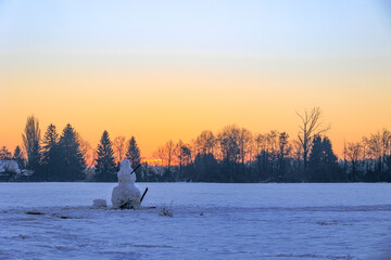A large snowman stands at sunrise on a snow-covered meadow in Siebenbrunn near Augsburg against a...