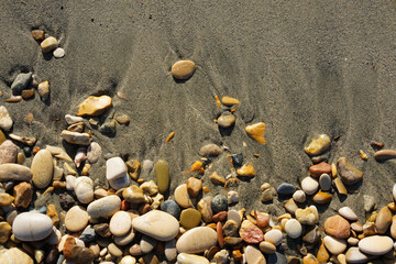 Fototapeta na wymiar Beautiful background of colorful stones on a sandy wet beach. the coast of Italy. Sea pebbles, top view