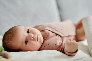 Close up shot of peaceful newborn with big blue eyes looking at camera and moving tiny hand while...