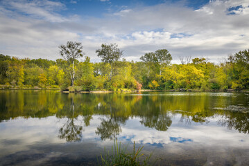 Scenic autumn lake with calm waters and mirror like reflection in the water and a blue sky with white clouds