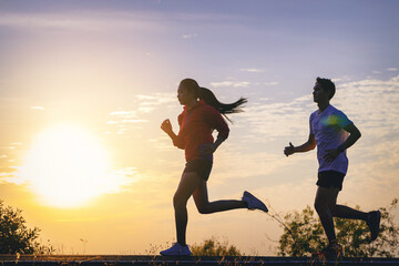 Young couples running sprinting on road. Fit runner fitness runner during outdoor workout with sunset background
