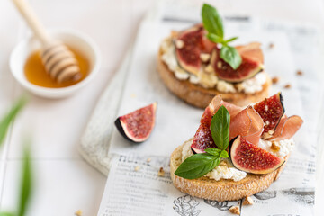 Delicious Bruschetta with prosciutto, creme cheese, figs, basil, walnut and honey on a wooden board. Antipasti, canape, crostini recipe, restaurant menu. Tasty breakfast. Side view, close up.
