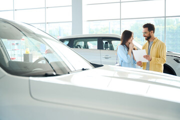 Joyful couple looking for new auto in car dealership