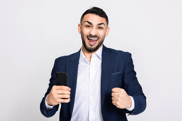 Handsome young buisnessman in ellegant smart suit costume over grey background in studio isolated celebrating the victory standing over grey background in studio isolated. Man trading gambling online.