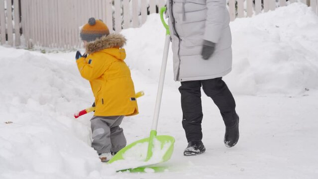 mother and child with shovels remove snow in the yard in winter. Winter kids fun outdoor, little helper removing snow with shovel