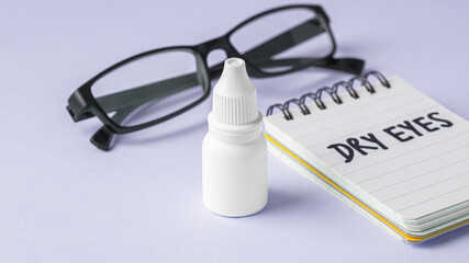 Eye drop bottle with eyeglasses and dry eyes word on notebook on pastel purple background