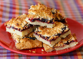 Crumble pie or cake with berry jam on red plate on multicolored towel blurred background. Homemade cakes.