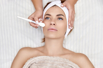 female hand touching the patient's face with a brush. beautician applies the mask to female face. facial skin care. top view