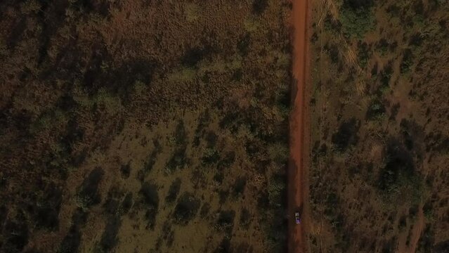 A drone follows a car driving along a dirt road