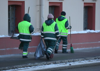 Three janitors with tools walk along a road cleared of snow, Fontanka River Embankment, St....