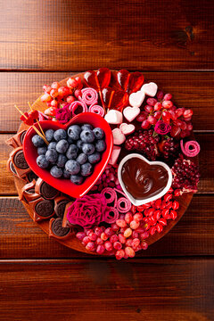 Snack board with berries, chocolate and sweets for Valentine's Day on a wooden background, top view vertical photo