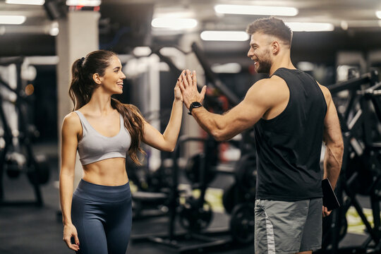 A fitness trainer is giving high five to a sportswoman in a gym.