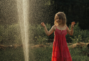 The girl plays in the summer in the garden, sprinkles with water, has fun - obrazy, fototapety, plakaty