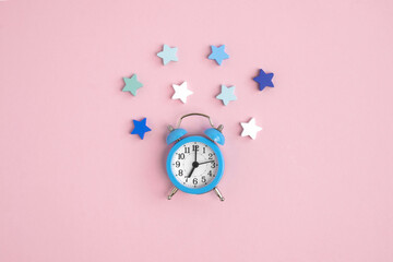 Blue alarm clock on a pink background, decorated with white, blue and green stars around. Bedtime...