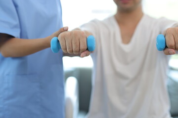 Nurse in an examination room at a hospital is doing physiotherapy for a male patient's arm with...