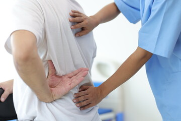 Doctor is diagnosing a male patient's back and lumbar pain in an examination room at a hospital.