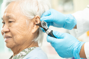 Audiologist or ENT doctor use otoscope checking ear of asian senior woman patient treating hearing loss problem.