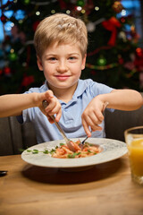 Cheerful boy enjoying festive dinner during New Year celebrating in restaurant