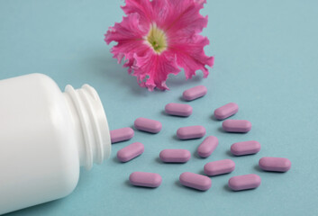 Oval purple pills spilled out of a white jar isolated on a blue color studio background. Mock-up....