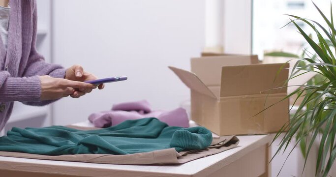 A woman selects clothes to donate and takes photos with her smartphone before sending them. Donation or recycling concept.