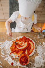 Adorable happy girl in chefs hat and apron cooking pizza at the kitchen