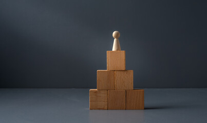 concept of being a winner ,wooden figure standing ontop of blocks , with a grey blue background . success in business ,