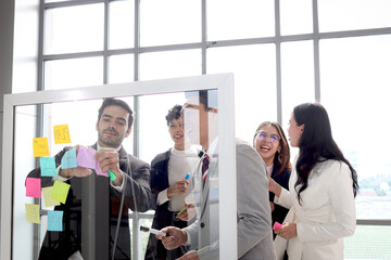 Businesspeople brainstorming at the meeting. Businessmen and businesswomen discussing, writing and putting paper note on summary chart glass board for creative idea, critical thinking teamwork,