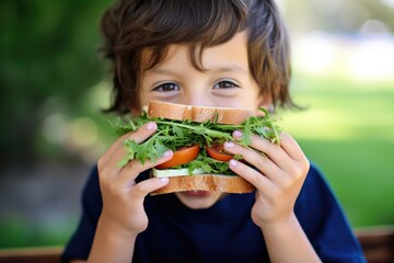 a child eating a humongous sandwich with fresh herbs - obrazy, fototapety, plakaty