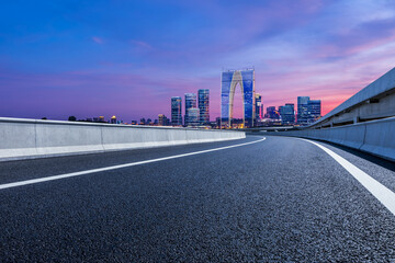 Asphalt road and city skyline with modern building at night in Suzhou, China. Road and city buildings background.