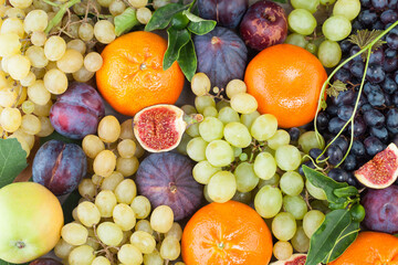 Apple, orange tangerine, figs and green and dark grape fruit mix with green leaves, healthy food background