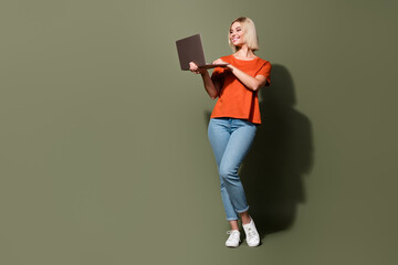 Full length photo of lovely young lady hold netbook secretary manager wear trendy orange garment isolated on khaki color background
