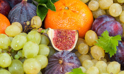Bright orange tangerine, figs and grape fruit mix with green leaves, healthy food background