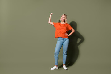 Fototapeta na wymiar Full length photo of lovely young lady raise fist flexing muscles wear trendy orange garment isolated on khaki color background