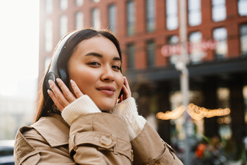 Smiling woman listening music with headphones while standing at city street