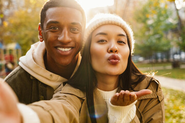 Happy couple taking selfie and blowing air kisses while standing in park