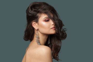 Naklejka premium Gorgeous stylish brunette woman jewelry model with long curly hair, healthy skin and earring closeup on blue background