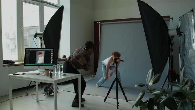 Time lapse of young male model walking in photo studio, posing on cyc wall background as Black female photographer taking pictures during fashion shoot