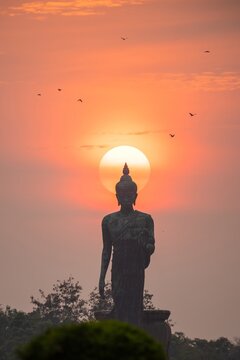 Stand big tall walk Buddha Statue in sun set Light background in park of thailand temple.Yellow orange light silhouette dark shadow of Buddha statue image Lord Buddha.